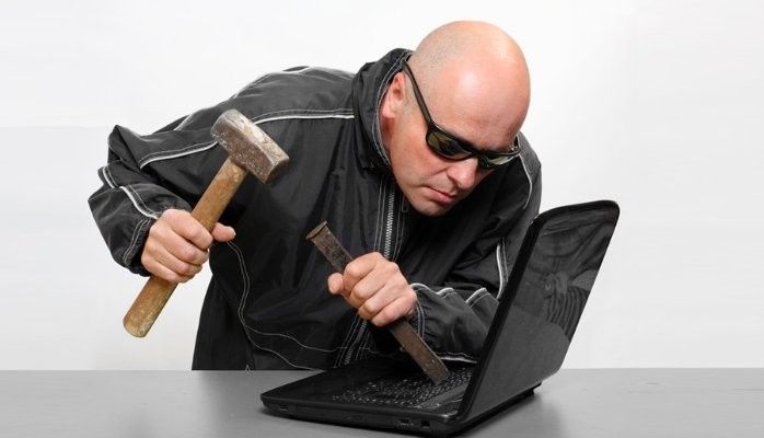 Man wearing all black hacking into a computer with a chisel