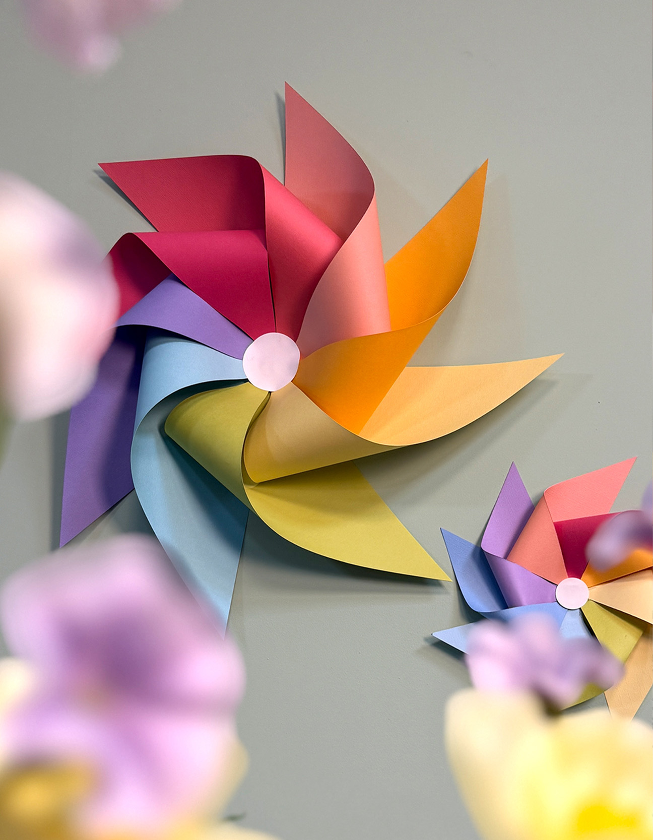 Colourful paper pinwheels in rainbow shades displayed decoratively on a wall.