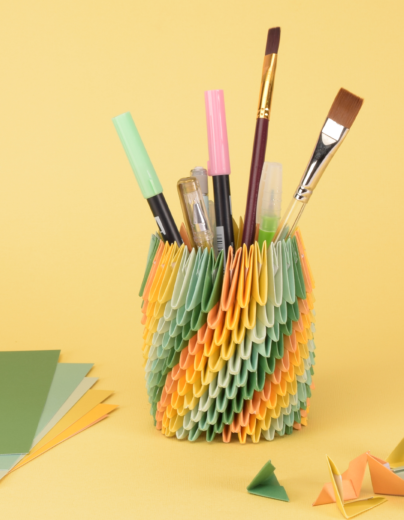 Fertiger farbenfroher Origami-Stifthalter mit Stiften und Pinseln auf einem Basteltisch.