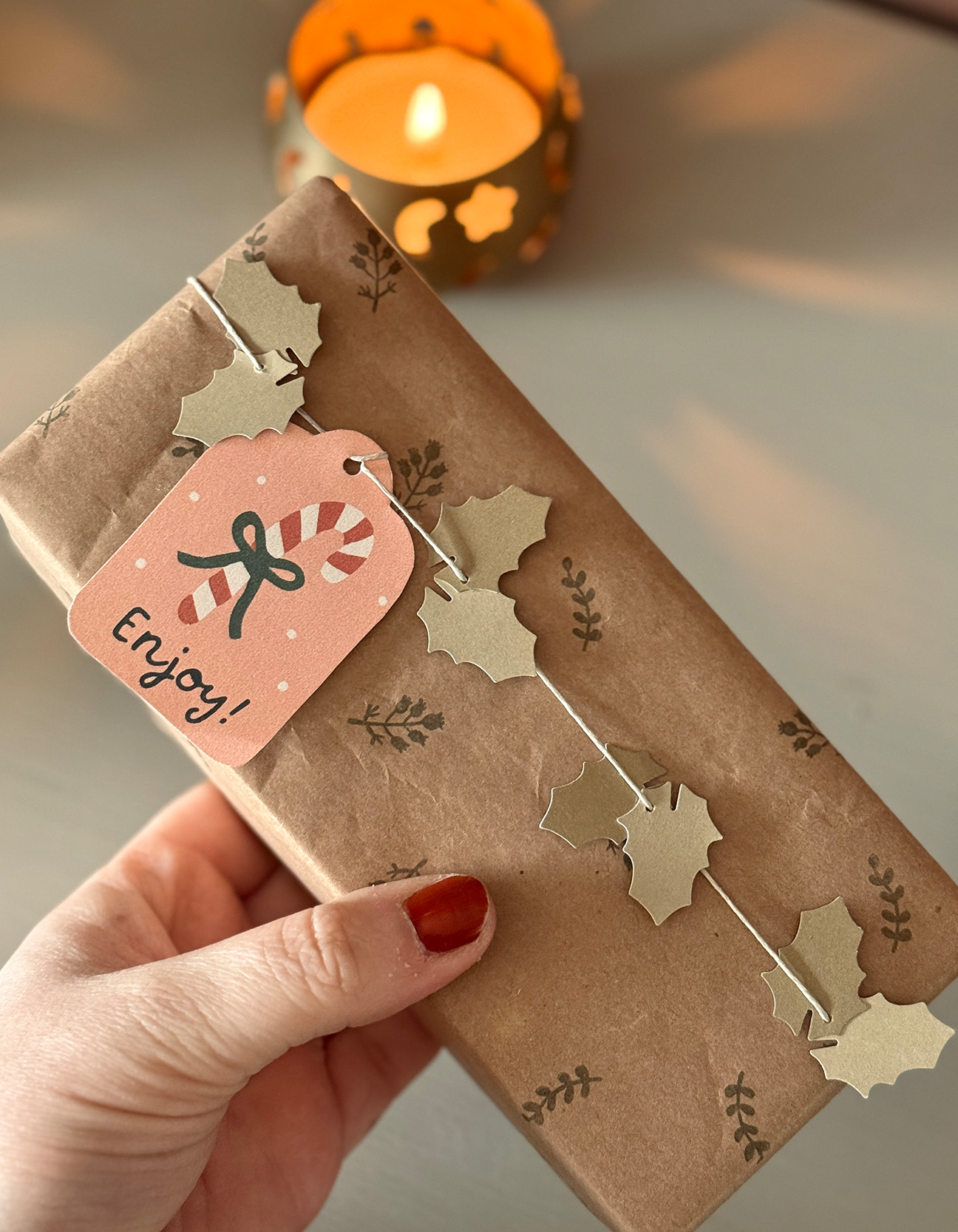 A festive Christmas gift wrapped with homemade holly leaf ribbon and a printed candy cane tag, ready for giving.