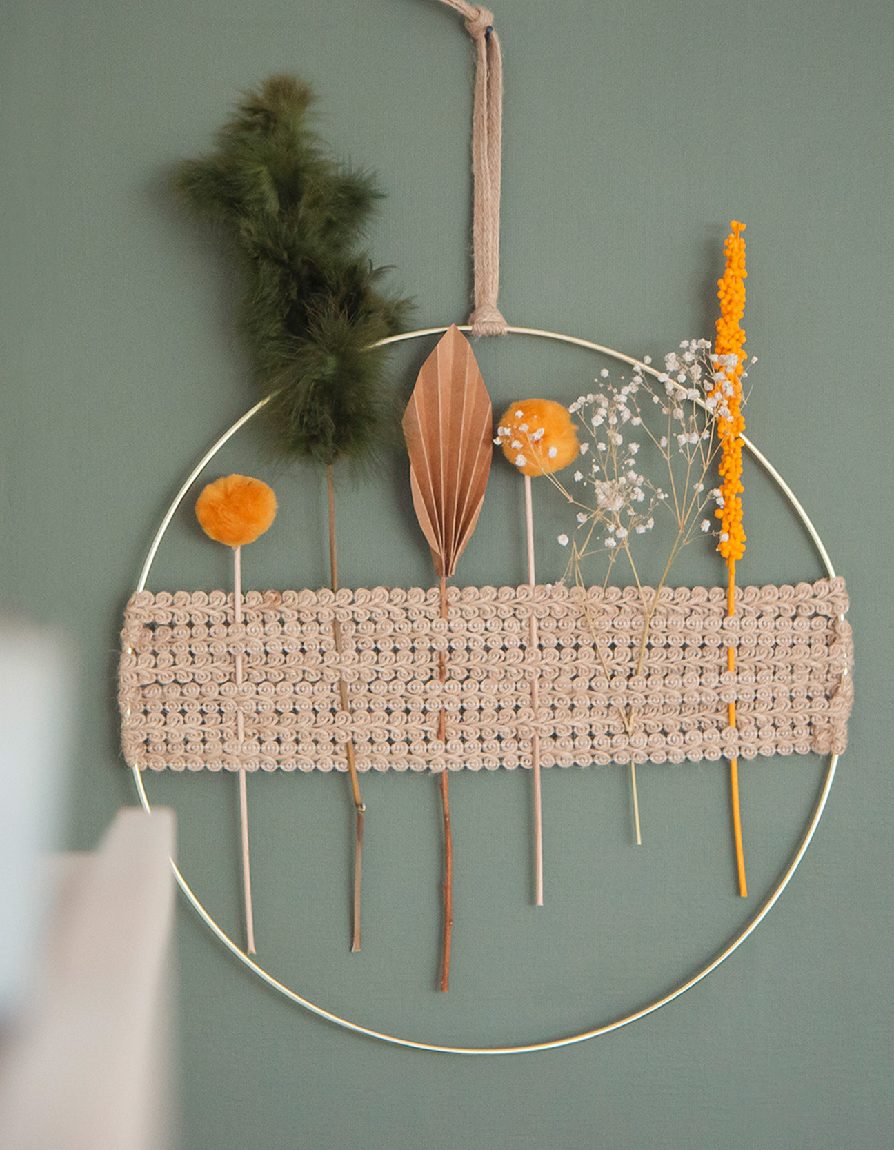 Finished DIY boho ring wall decoration featuring jute ribbon, dried flowers, feathers, and handmade botanical elements in a modern natural interior.