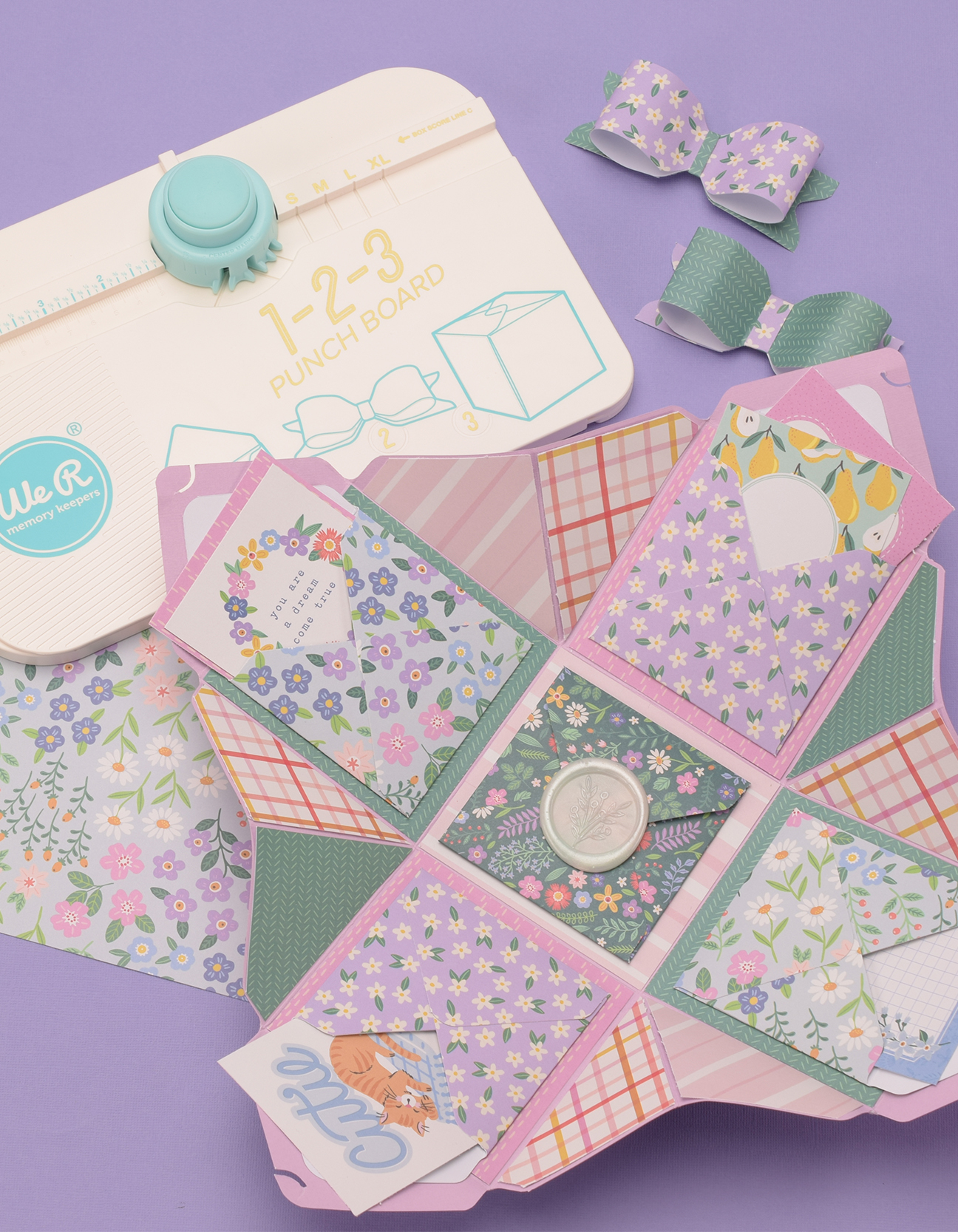 Fertige DIY-Explosionsbox aus gemustertem Scrapbookpapier, die sich zu einer dekorativen Überraschungsbox mit Taschen und handgemachter Schleife öffnet.