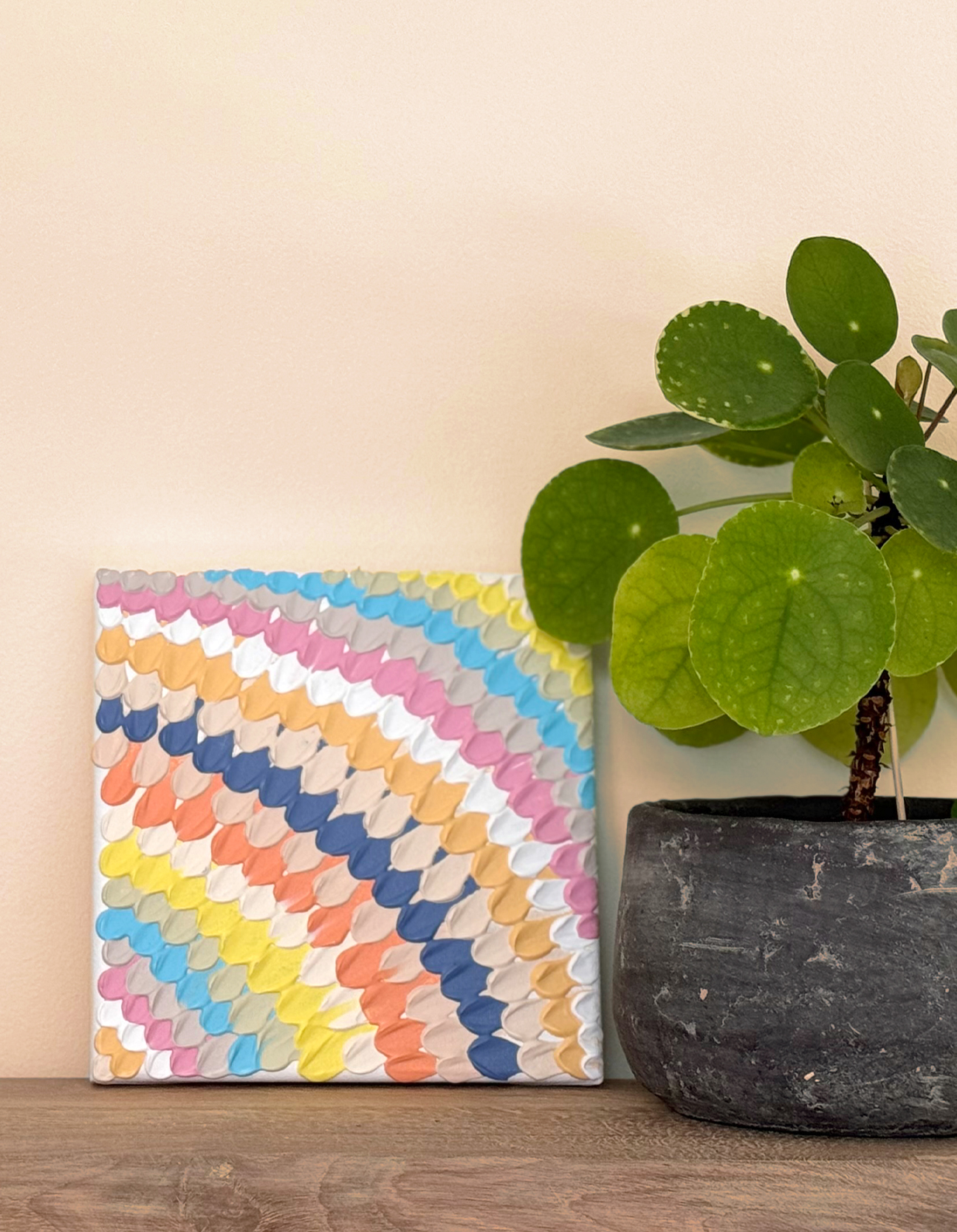 Tableau acrylique coloré et texturé posé sur étagère à côté d’une plante verte