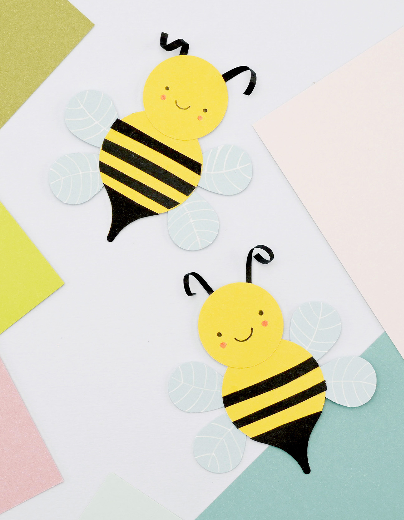 Finished DIY paper bees with blue wings, yellow bodies and black stripes on a pastel background