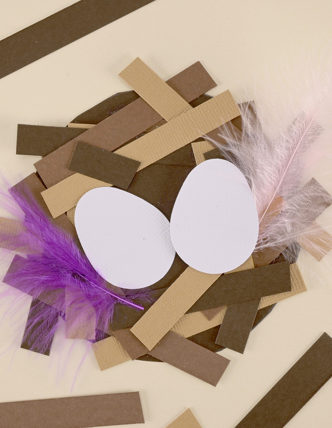 Fertiges DIY-Papier-Vogelnest mit weißen Eiern und weichen Federn aus braunem Tonkarton als Frühlingsdeko.