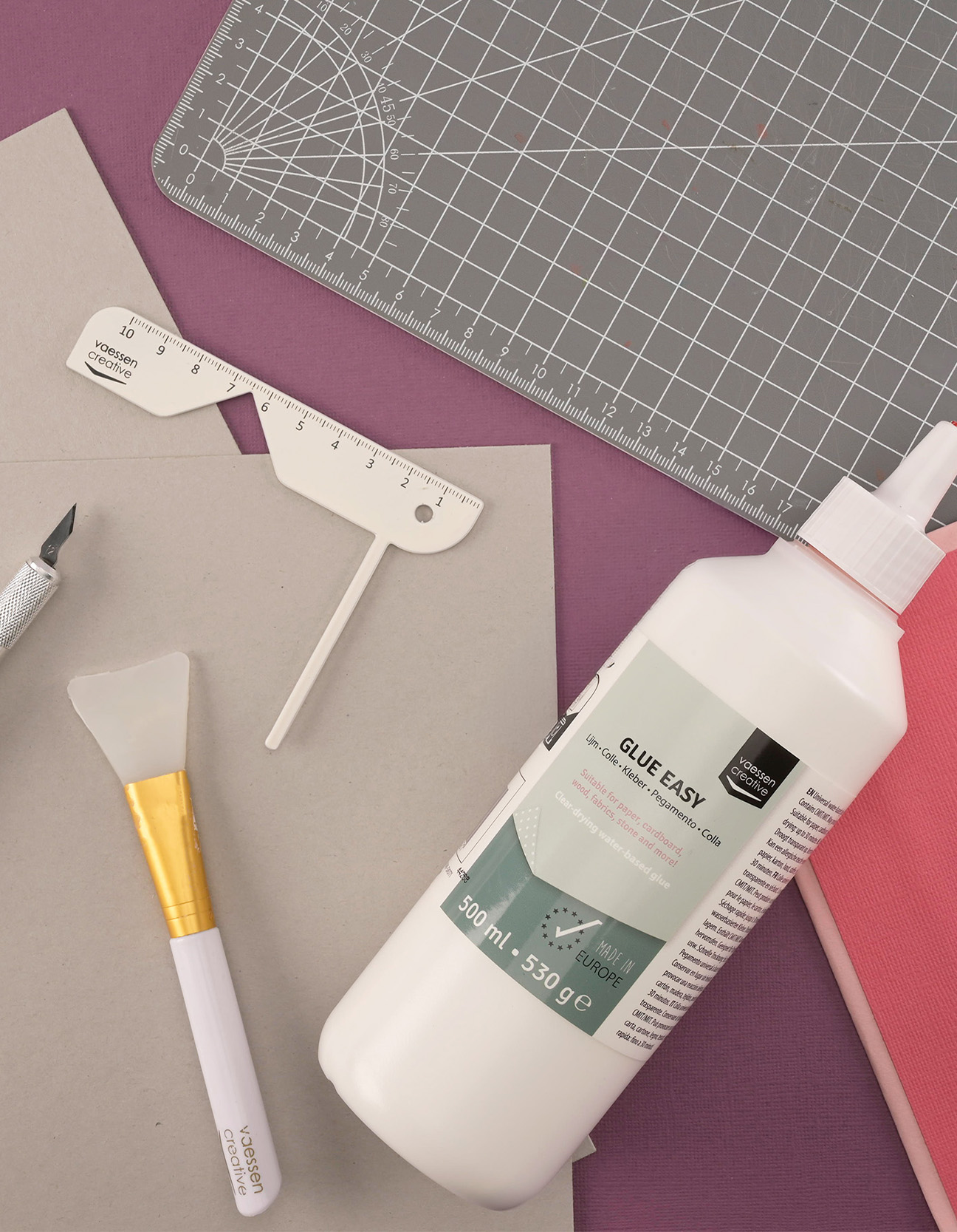 Materiales para hacer una cubierta de libro resistente con cartón gris, pegamento, papel y herramientas