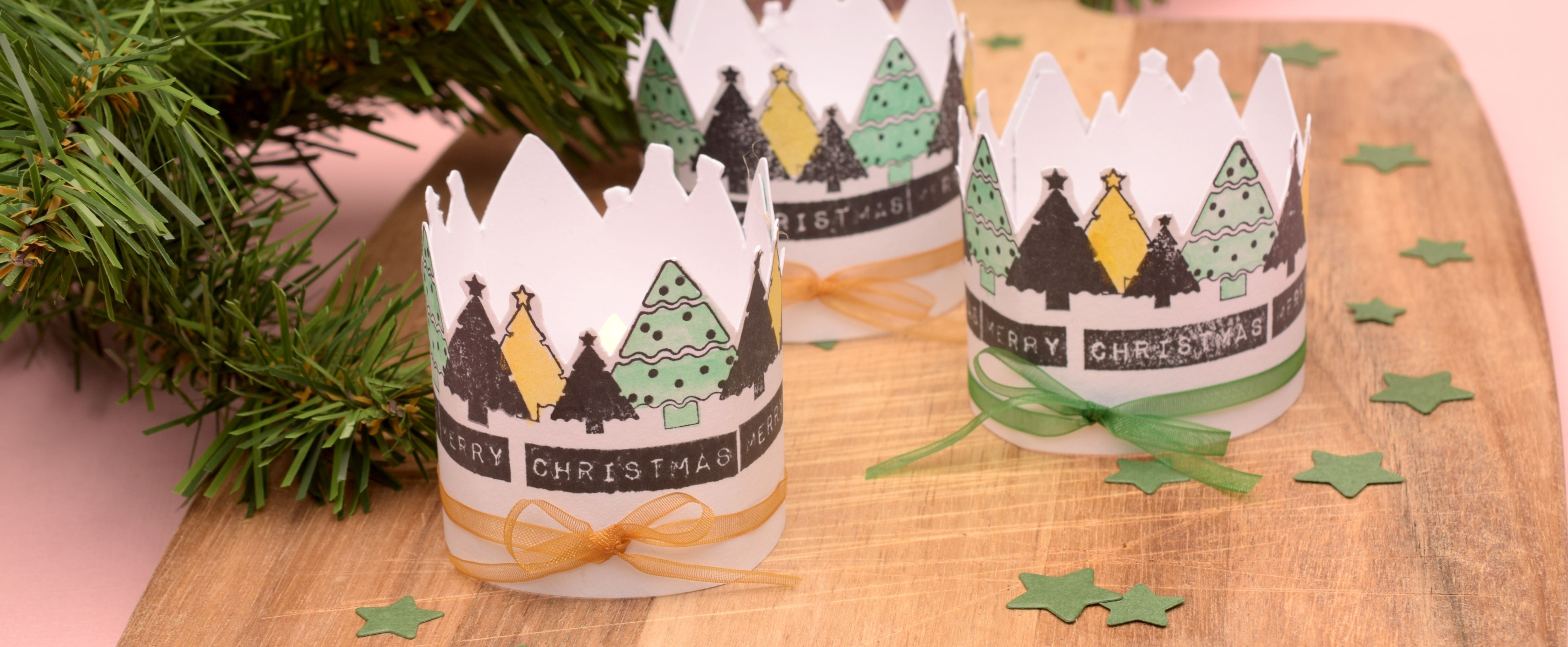 Portacandele natalizi fai-da-te con alberi di carta timbrati e colorati e fiocchi di nastro.