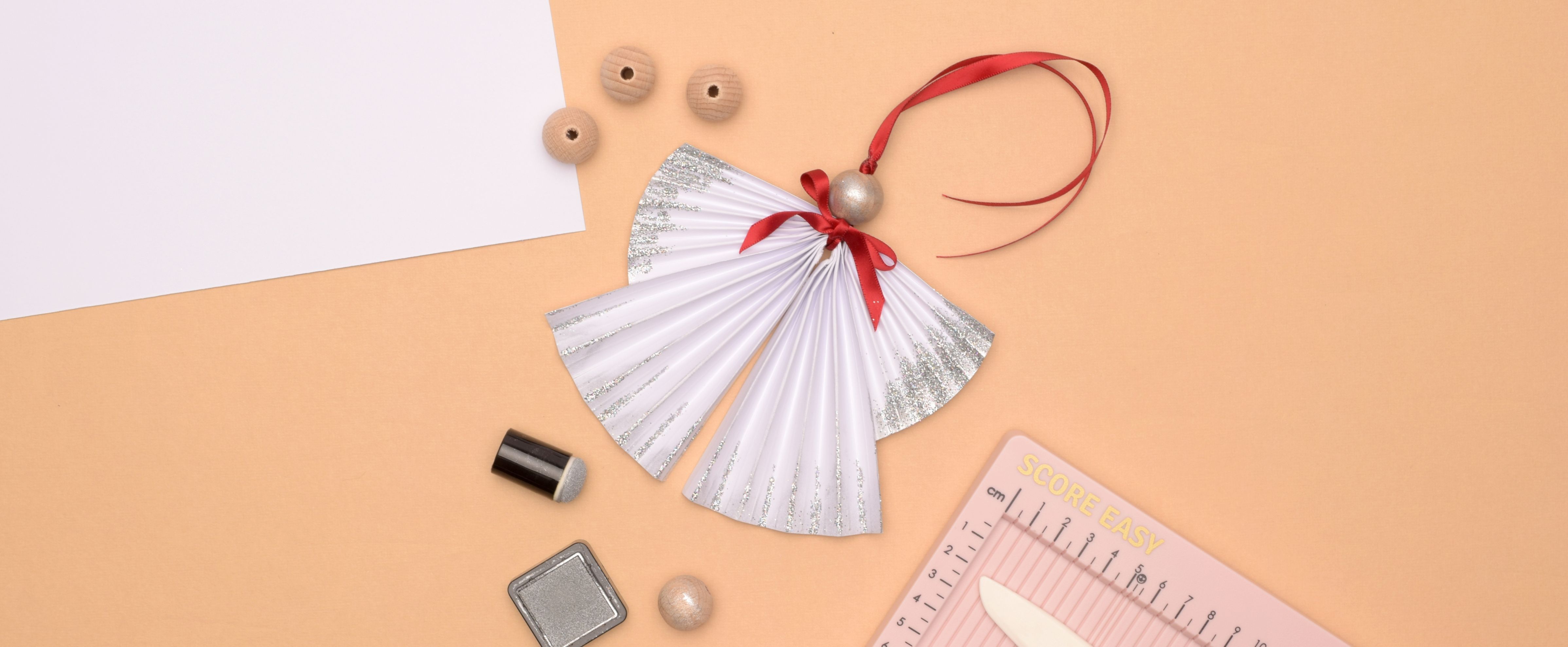 Adorno de ángel de papel – clásico ángel navideño con purpurina y cinta, símbolo de paz y luz.