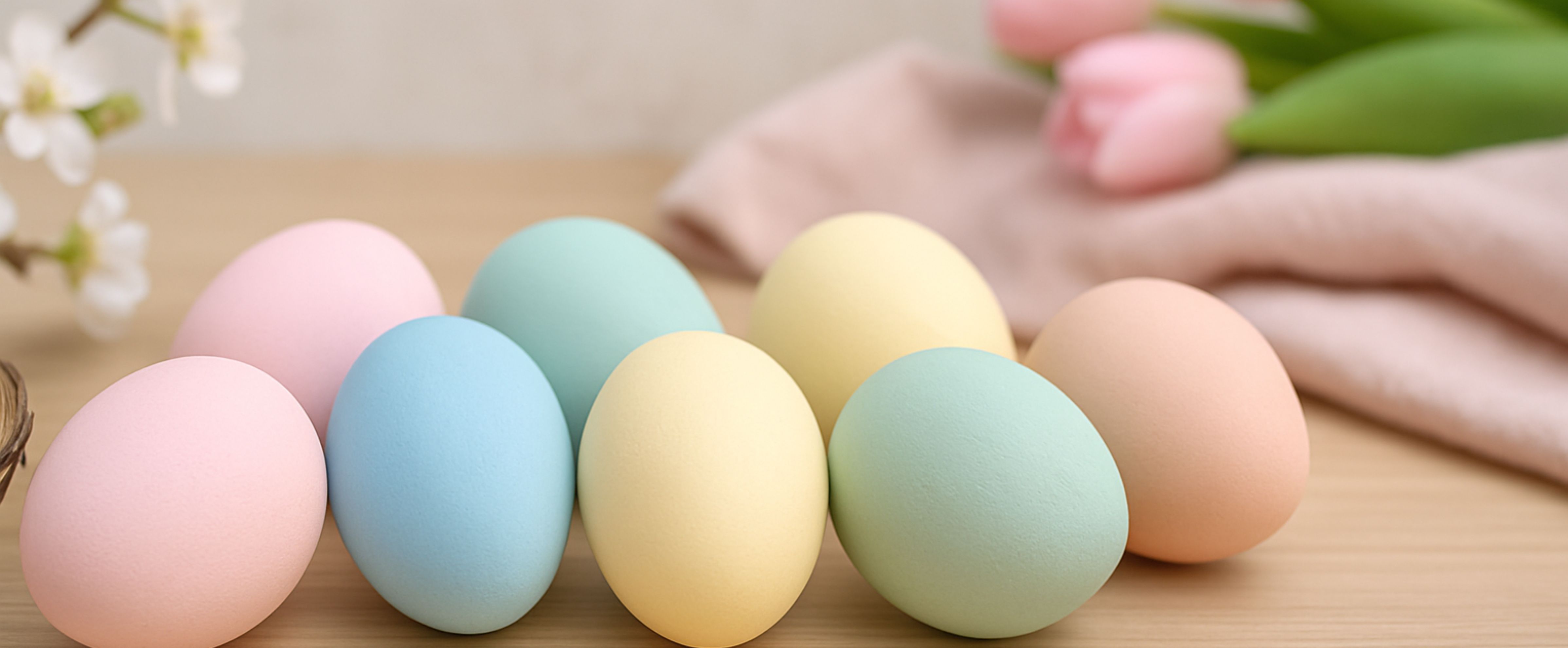 Œufs de Pâques aux couleurs pastel posés sur une surface en bois avec une douce décoration printanière en arrière-plan.