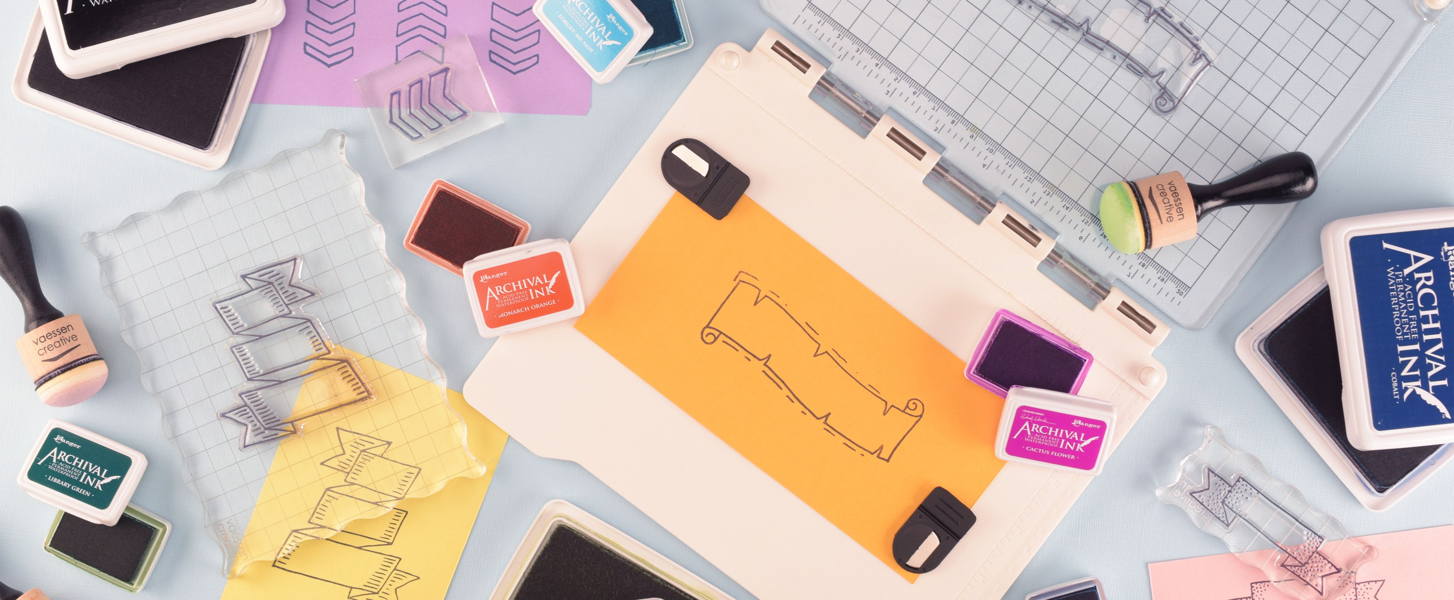 Basic materials for stamping on a craft table, including ink pads, clear stamps, acrylic blocks, daubers and a stamp platform with a stamped banner design.