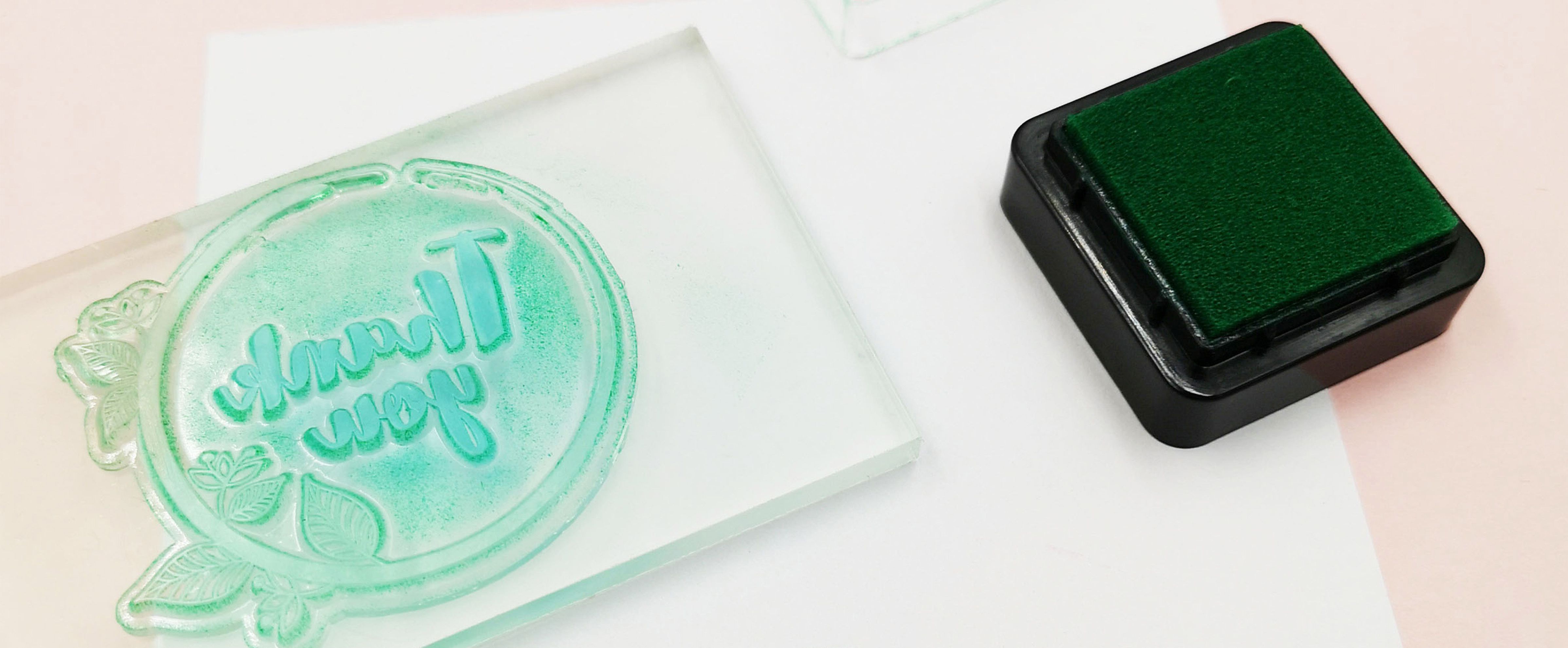 Decorating gift tags with stamps using a green ink pad and a clear “Thank you” stamp on an acrylic block above white cardstock.