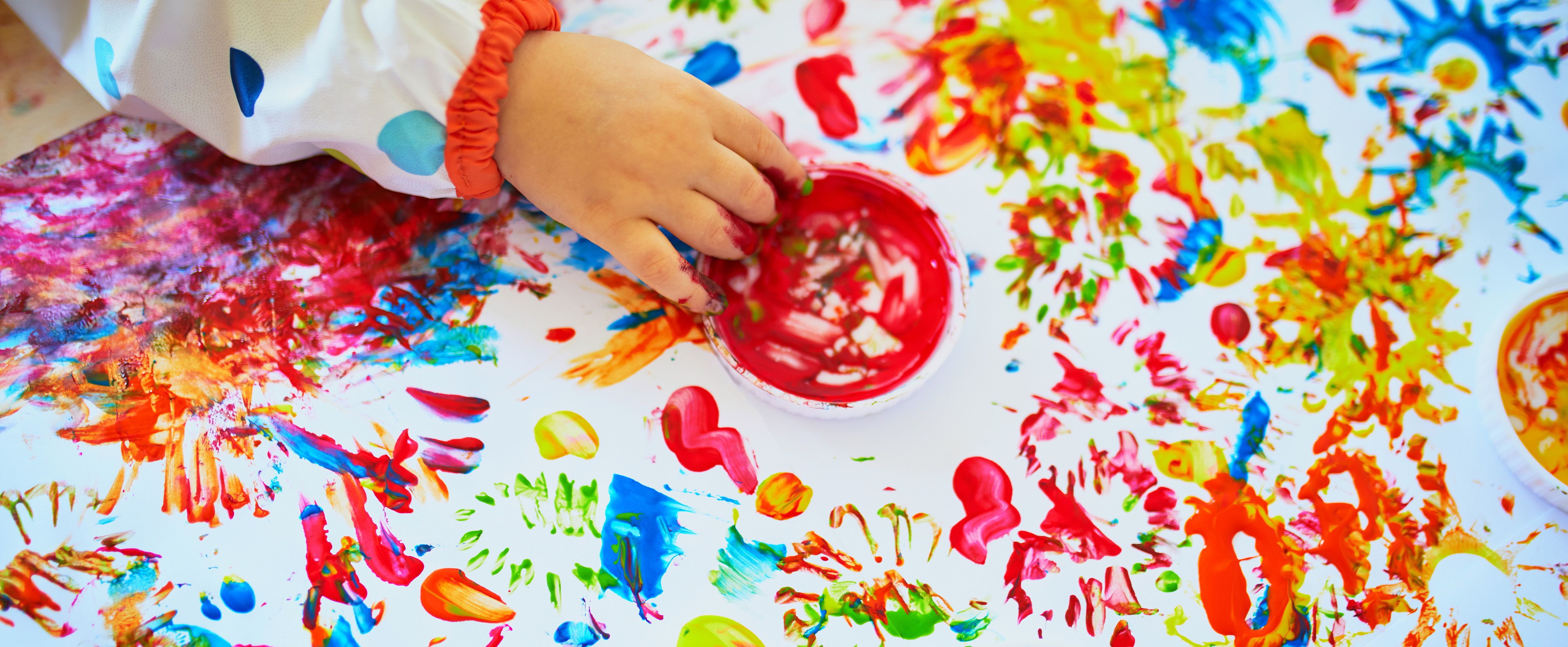 Basteln mit Kleinkindern beim Fingermalen auf einem großen Blatt Papier mit leuchtend roter, gelber und blauer Farbe.
