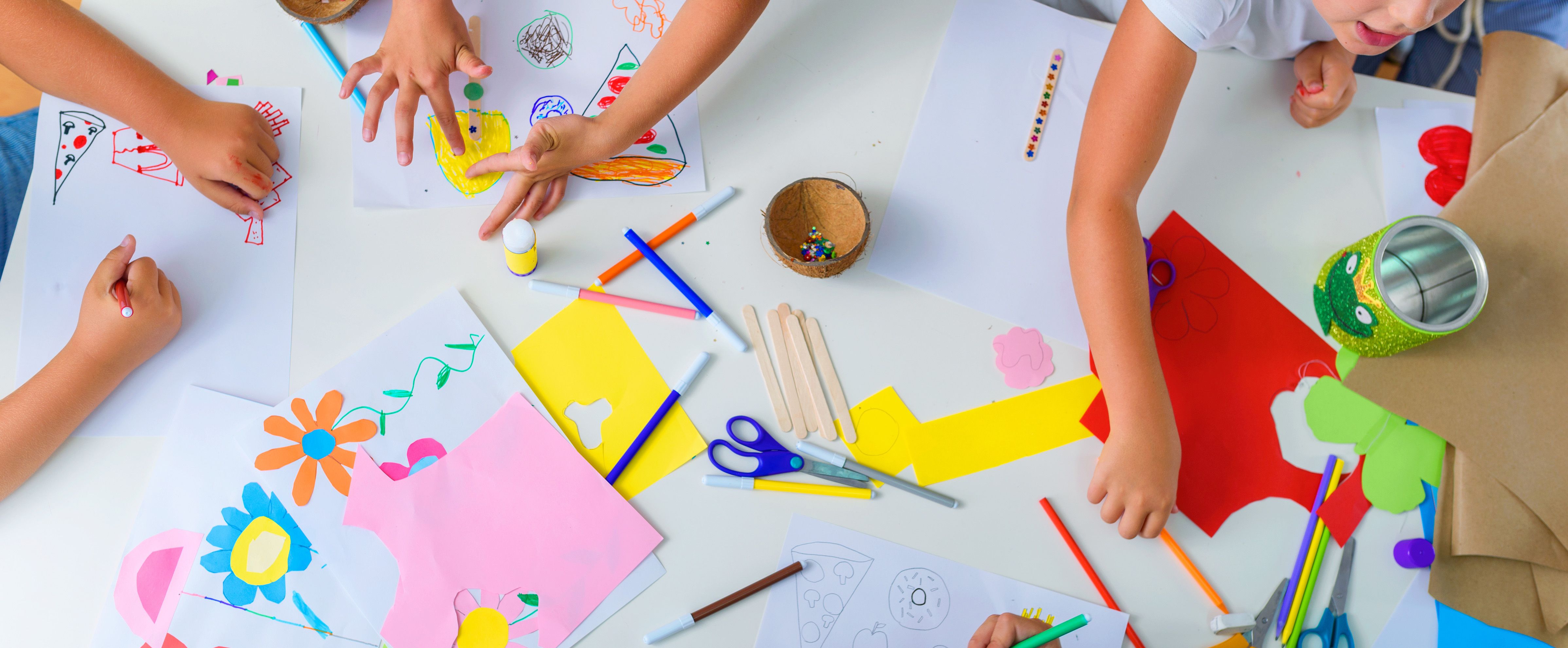 Basteln mit Kleinkindern am Tisch mit Papier, Filzstiften, Kleber, Scheren und bunten Verzierungen.