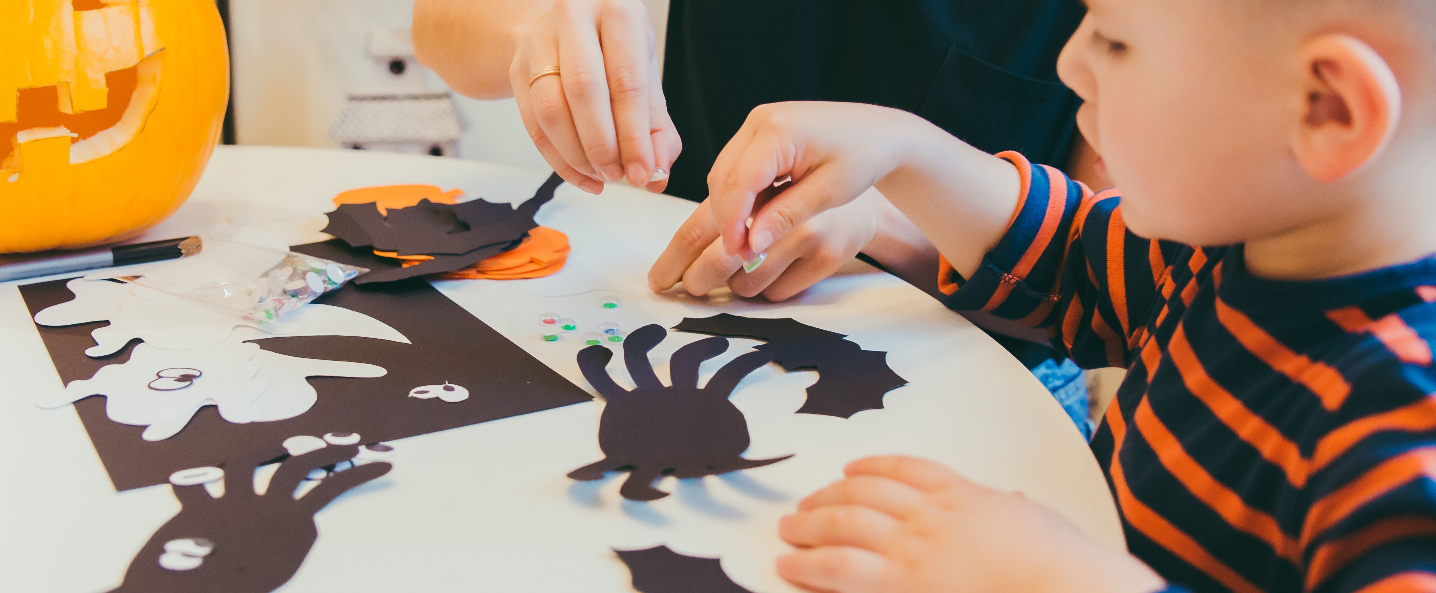 Basteln mit Kleinkindern im Herbst mit Papierspinnen, Fledermäusen, Gespenstern und Wackelaugen am Tisch.