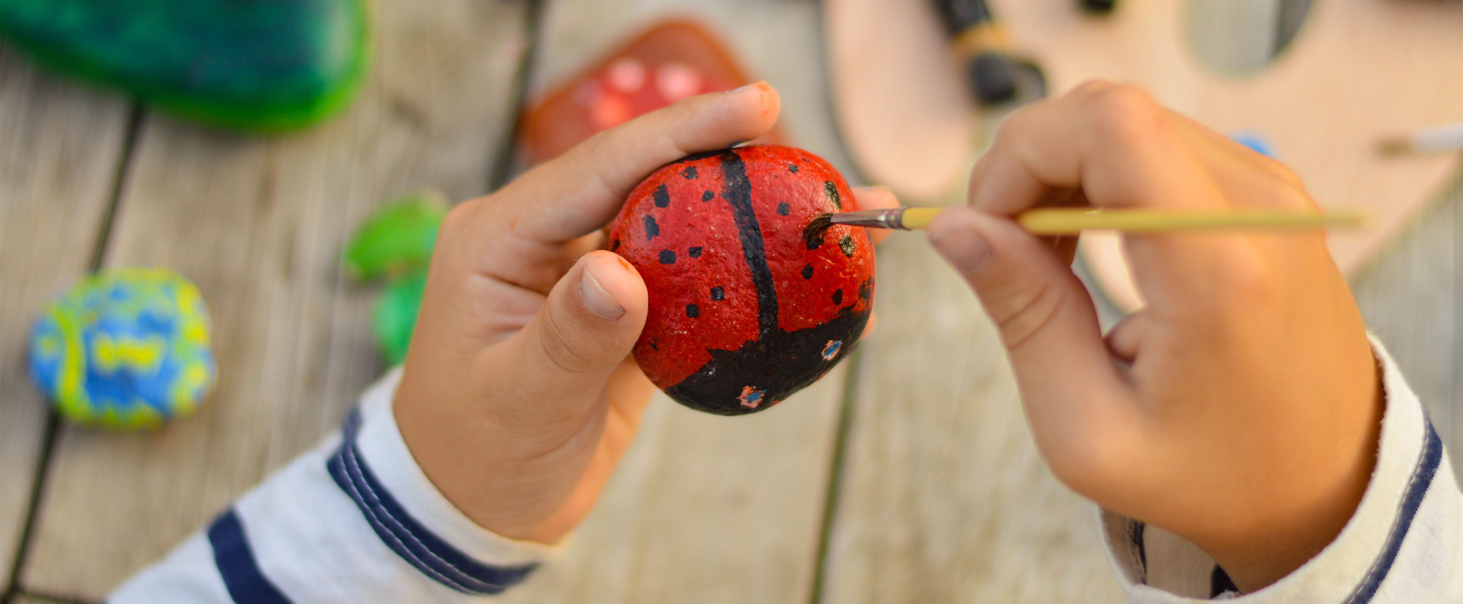 Crafting with preschoolers: child painting a ladybird on a stone with a small brush.