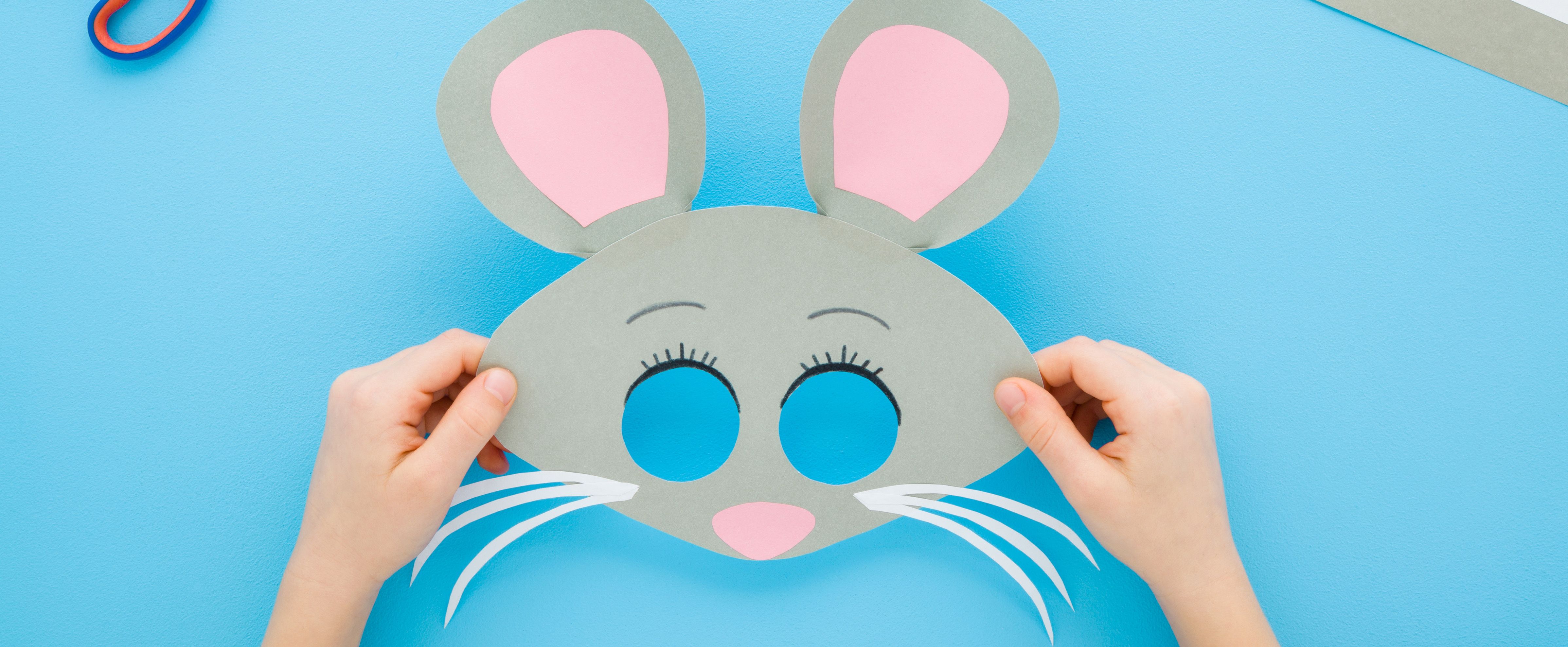 Crafting with preschoolers: handmade paper mouse mask held by a child on a blue background.