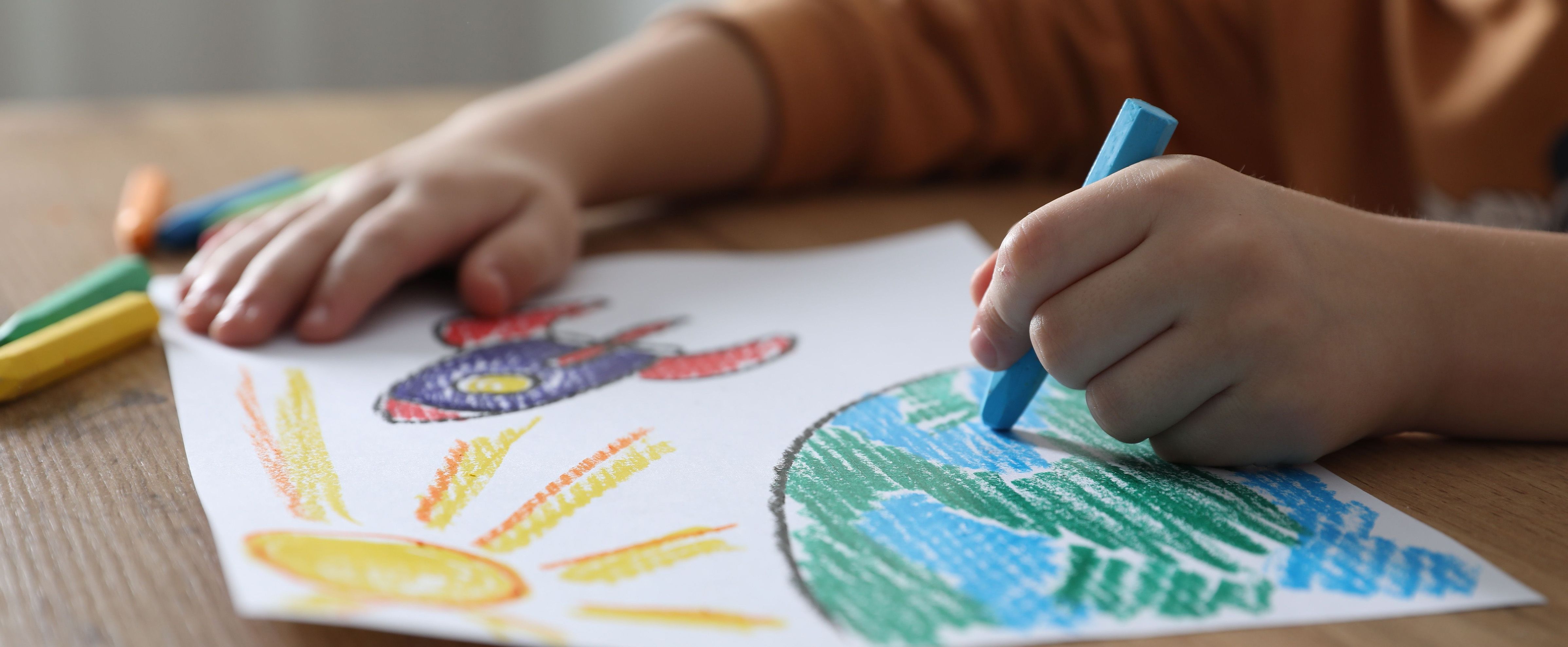 Niño coloreando un dibujo del espacio con ceras, una idea de manualidades para chicos con cohetes y planetas