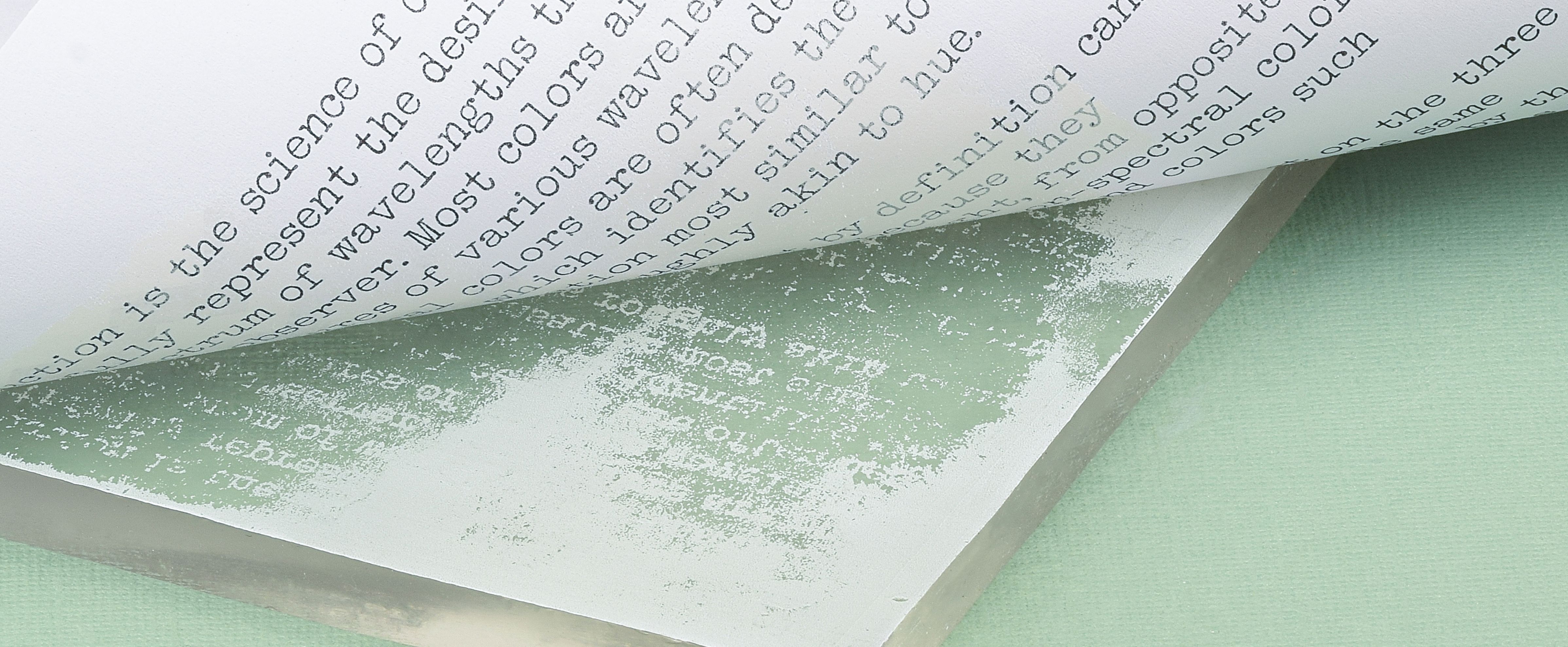 Pulling a paper print from a gel printing plate with green paint and transferred text texture