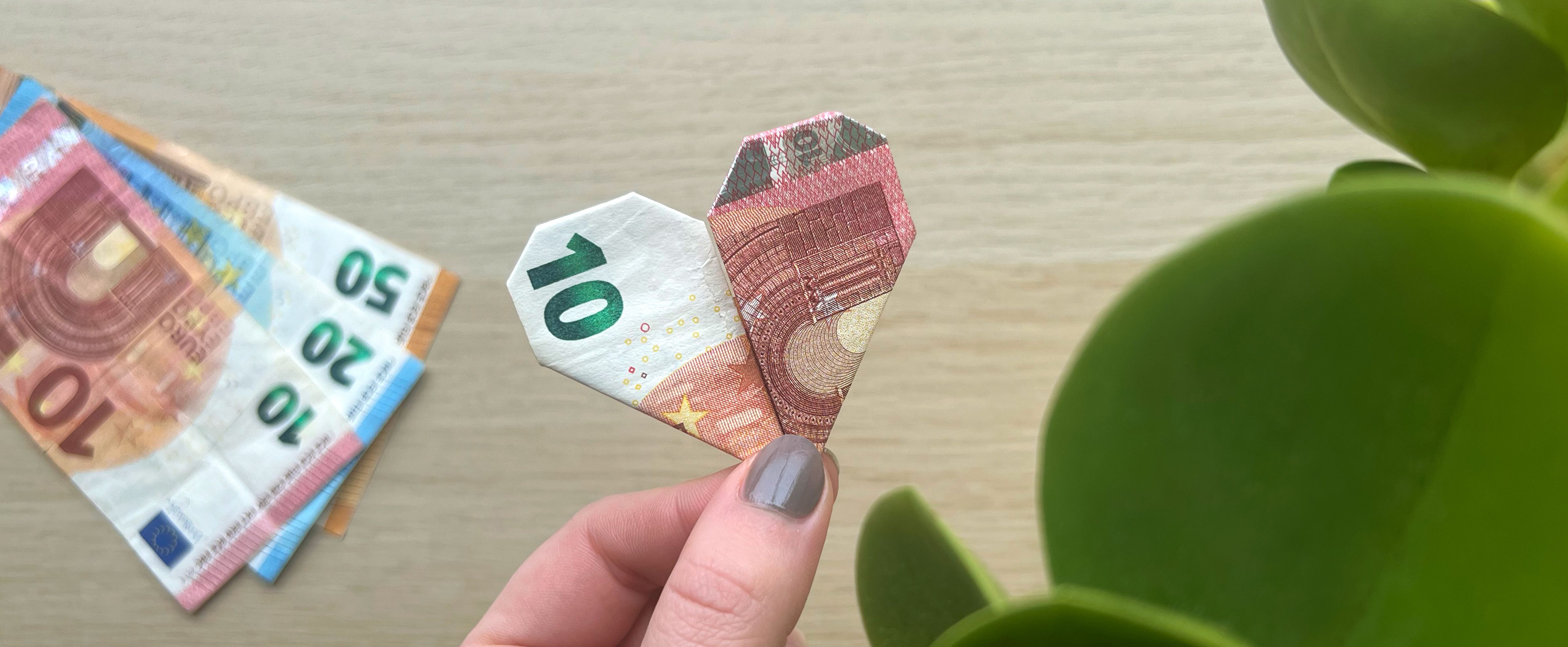 Folded money heart made from euro banknotes, held between fingers as a creative DIY gift idea.