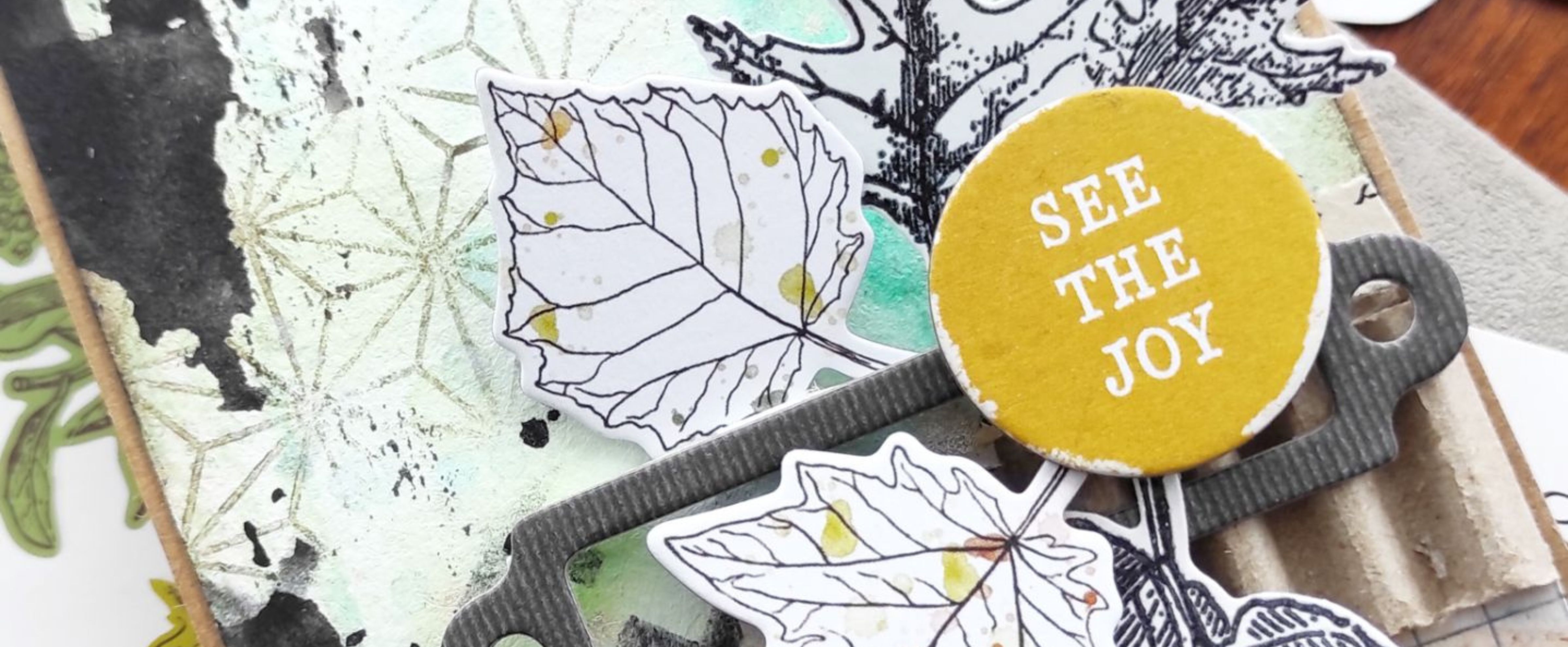 Close-up of a mixed media card with Gel Press background, stamped leaves and yellow See the Joy embellishment