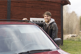 Smiling man standing behind a car