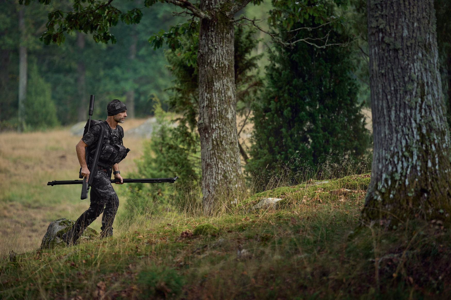 Jäger mit Tarnkleidung und Ausrüstung bei der Pirsch im grünen Wald.png