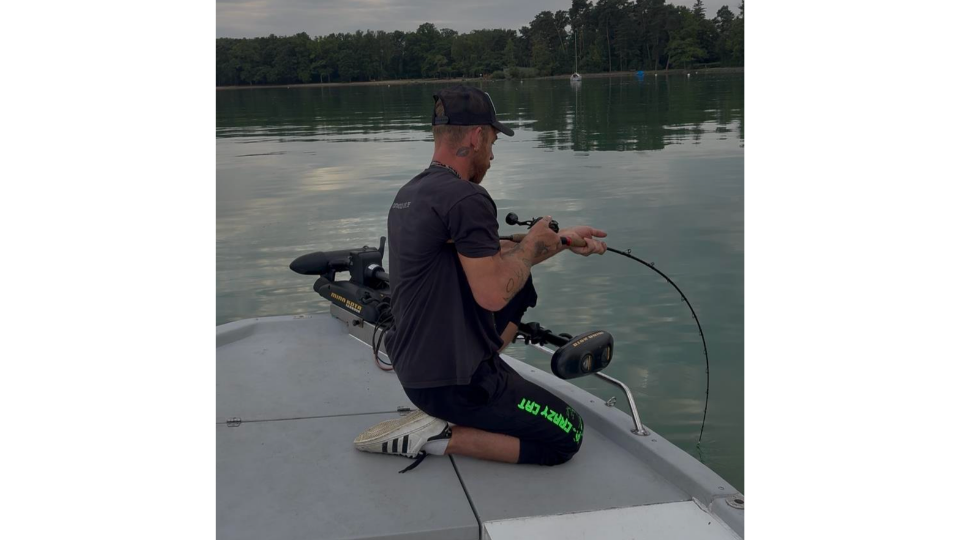 Tinu kniet am Bootsrand und drillt einen Wels, während sich die Vollcarbon-Wallerrute extrem nach unten ins Wasser biegt.png
