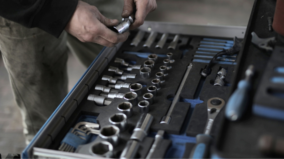 Nahaufnahme von Händen eines Handwerkers, der einen Steckschlüsseleinsatz aus einer ordentlich sortierten Schublade eines Werkstattwagens wählt.png