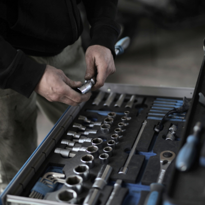 Nahaufnahme von Händen eines Handwerkers, der einen Steckschlüsseleinsatz aus einer ordentlich sortierten Schublade eines Werkstattwagens wählt.png