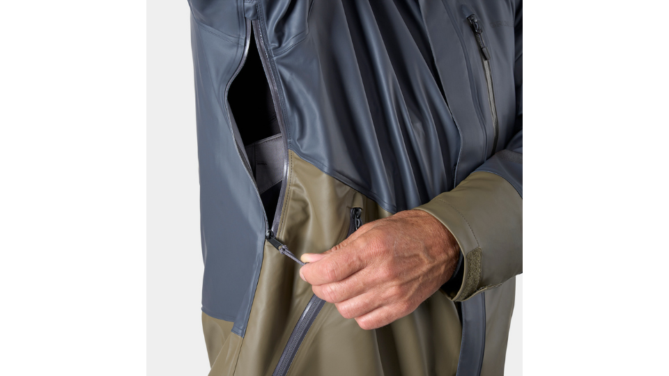 Gros plan sur une veste de pluie bleu marine de Grundéns. Une main actionne la fermeture éclair latérale idéalement placée pour offrir une liberté de mouvement maximale pendant la pêche.png