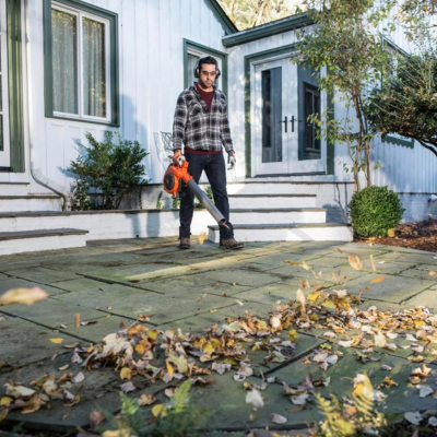Mann reinigt eine Terrasse vor dem Haus mit einem orangefarbenen Husqvarna Laubbläser im Herbst.png