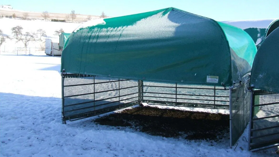 Abri de prairie vert avec structure métallique offrant une protection contre les intempéries sur un pâturage enneigé en hiver.png