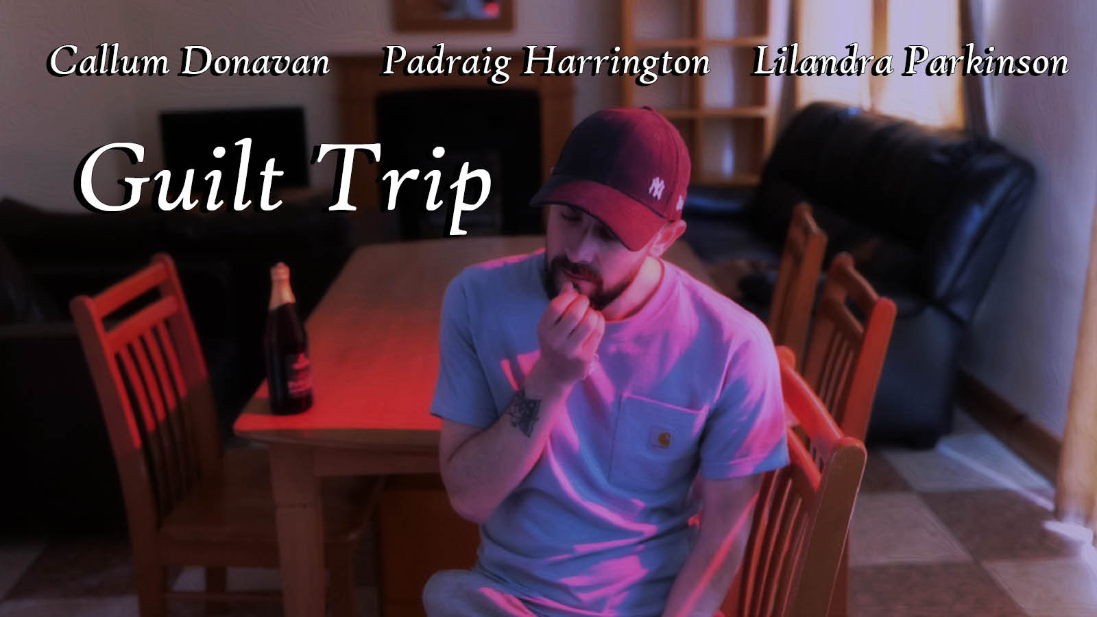 Young man sitting at a table in a kitchen with his hand to his face and a bottle of beer on the table. Name of film Guilt Trip is on the image and the actors names Callum Donavan, Padraig Harrington, and Lilandra Parkinson are on the image