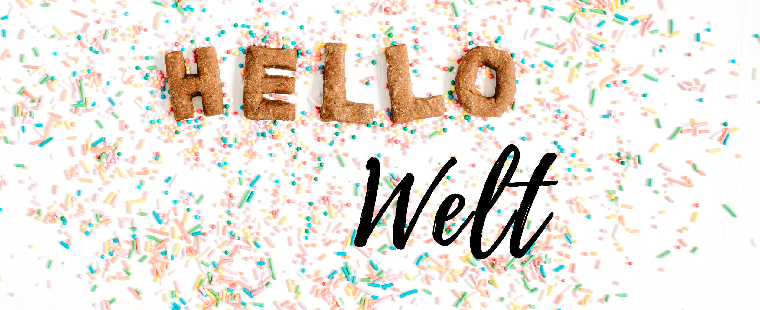 Kekse mit der Aufschrift HELLO und dem Wort Welt darunter, umgeben von bunten Streuseln auf weißem Hintergrund.