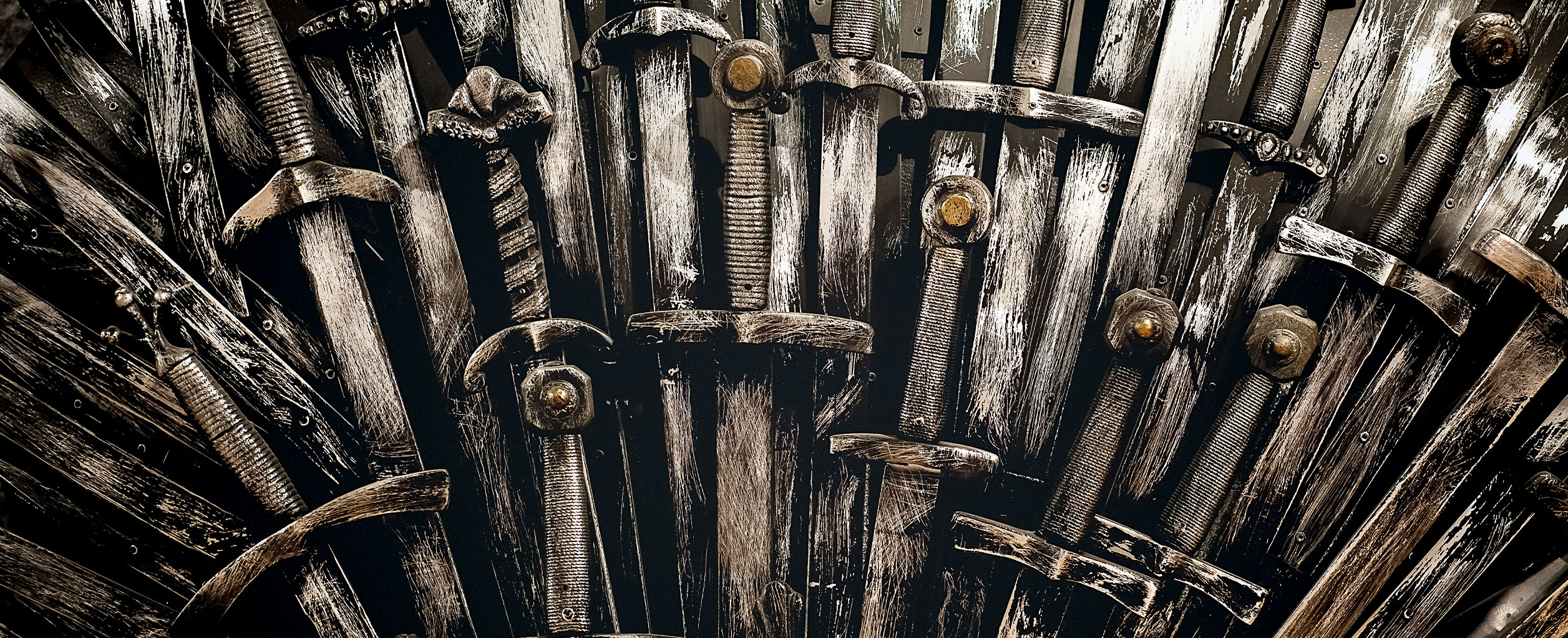 Eine Nahaufnahme von sich überlappenden Schwertern im mittelalterlichen Stil, die vertikal angeordnet sind, mit verwitterten Metallklingen und verzierten Griffen.