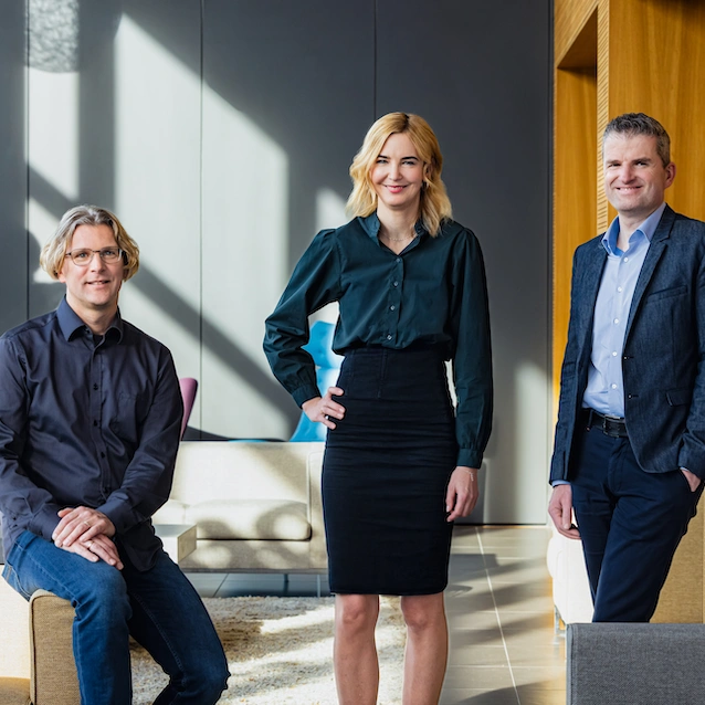 Die drei Vorstandsmitglieder Lars, Verena und Rainer stehen zusammen und lächeln in die Kamera