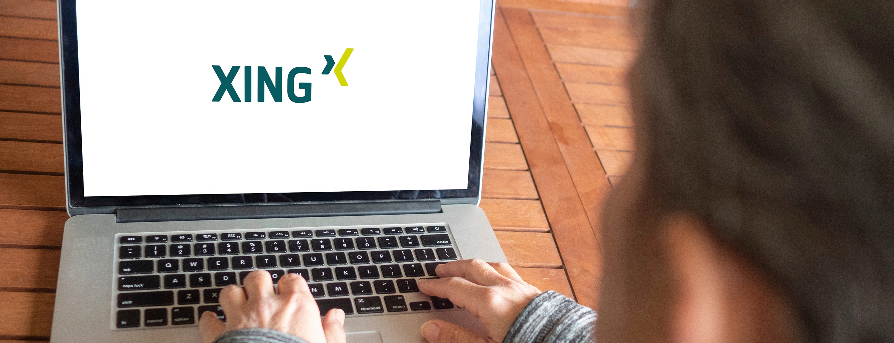 Eine Person die auf einem Laptop etwas tippt, auf welchem ein XING Logo auf weißem Hintergrund zu sehen ist.