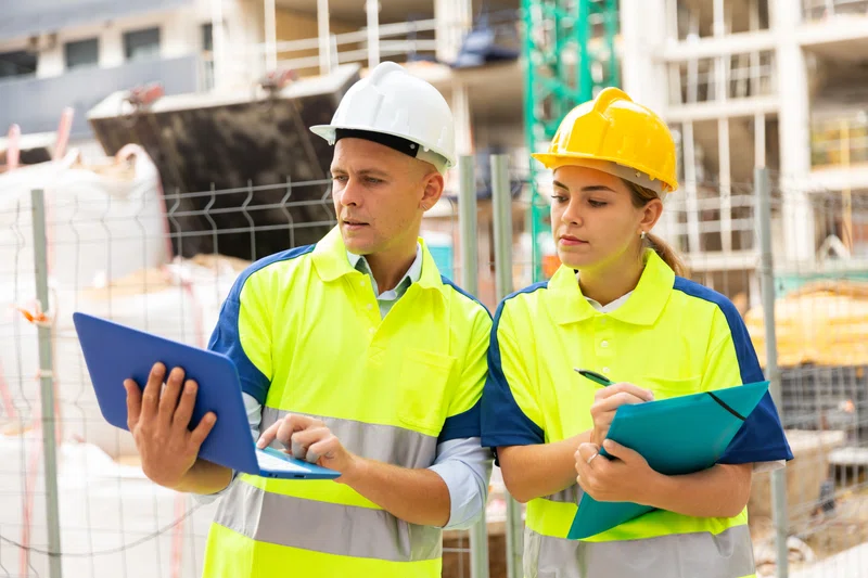 Man and woman looking at laptops on a building site