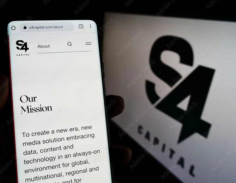 Person holding cellphone with website of UK advertising company S4 Capital plc on screen in front of logo