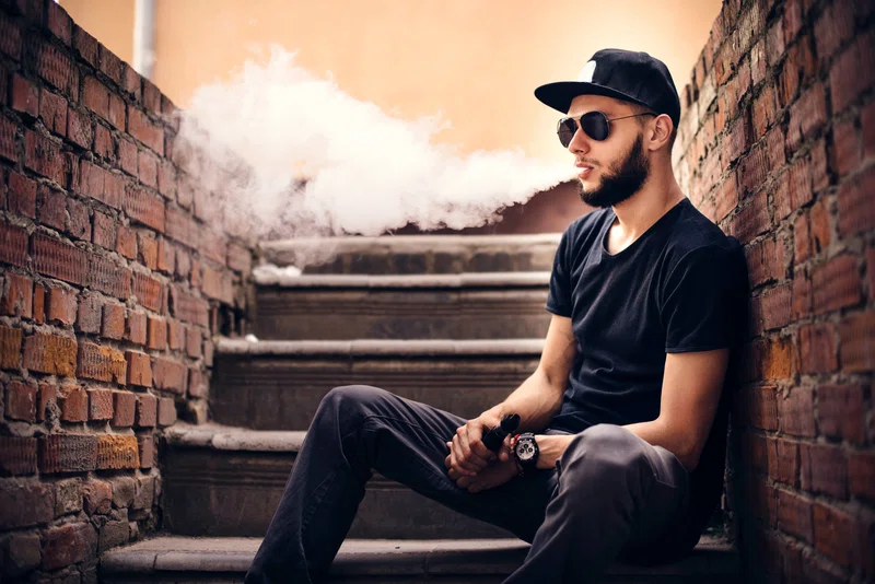 Young adult sitting on steps blowing out smoke from vaping