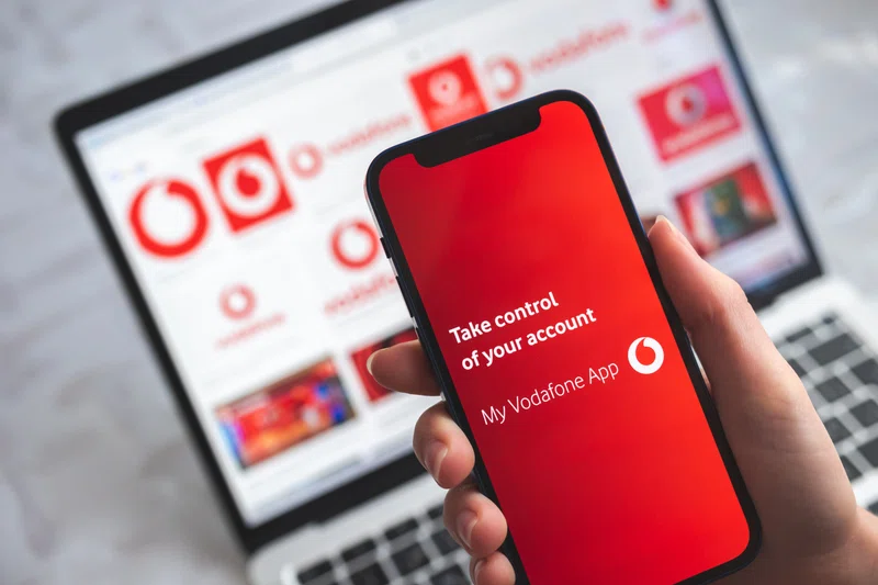 Smartphone showing Vodafone app against company branded laptop background