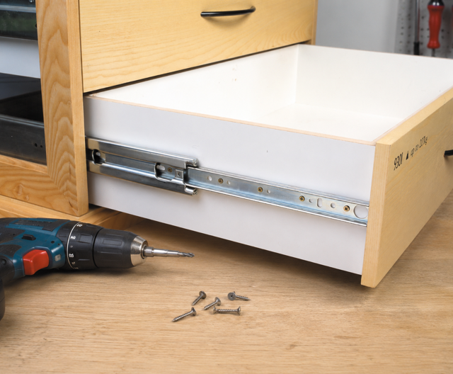 Installing metal drawer slides on a drawer using a drill and screws