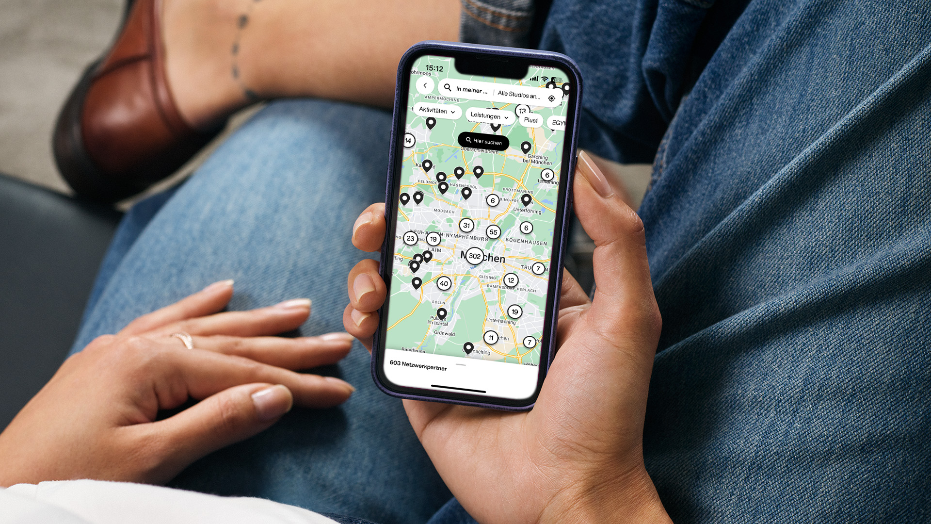 Nahaufnahme einer Person, die auf einem Smartphone die EGYM Wellpass App mit einer Standortkarte von München nutzt und sich das passende Partnerstudio für ihren Bedarf aussucht.