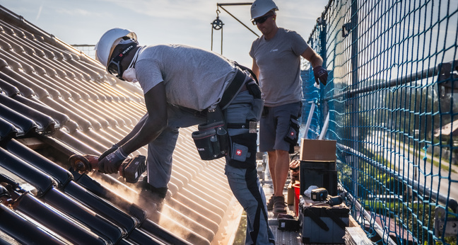 Zwei Handwerker arbeiten auf einem Dach an einer Photovoltaikanlage bei sonnigem Wetter – Einsatz im Bereich Solarenergie und Gebäudetechnik.