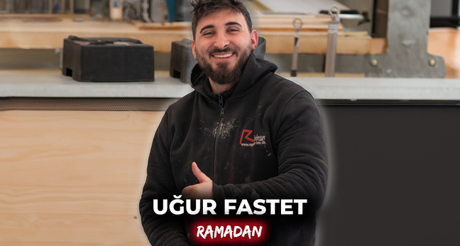 Dachdeckergeselle Ugur Uyar lächelt in Arbeitskleidung in einer Werkhalle – sein Arbeitgeber unterstützt ihn während des Ramadans, was kulturelle Vielfalt am Arbeitsplatz sichtbar macht.