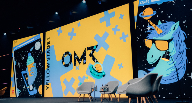 Blick auf die Yellow Stage beim OMR Festival mit leuchtend gelbem Bühnenbild, auffälliger Einhorn-Illustration und moderner Sitzgruppe – eine der zentralen Festivalbühnen für Keynotes und HR-Formate.