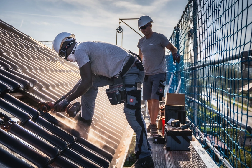 Zwei Handwerker arbeiten auf einem Dach an einer Photovoltaikanlage bei sonnigem Wetter – Einsatz im Bereich Solarenergie und Gebäudetechnik.