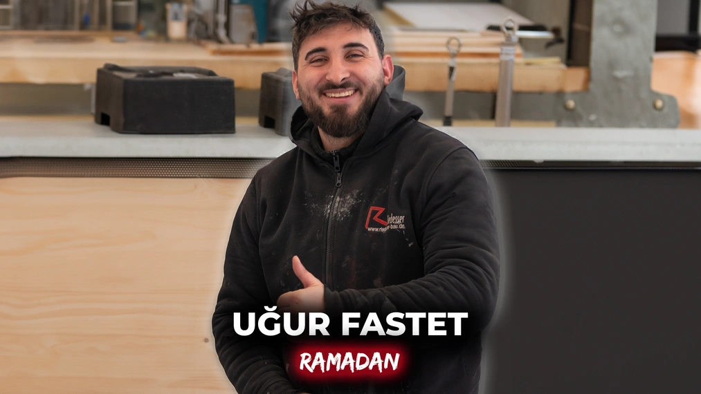 Dachdeckergeselle Ugur Uyar lächelt in Arbeitskleidung in einer Werkhalle – sein Arbeitgeber unterstützt ihn während des Ramadans, was kulturelle Vielfalt am Arbeitsplatz sichtbar macht.