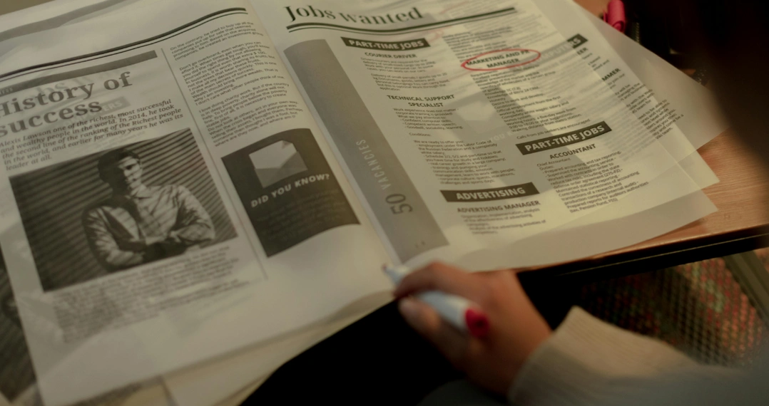Zu sehen ist eine aufgeschlagene Zeitung in der Stellenausschreibungen inseriert sind. Dort wurde ein rot markiert.