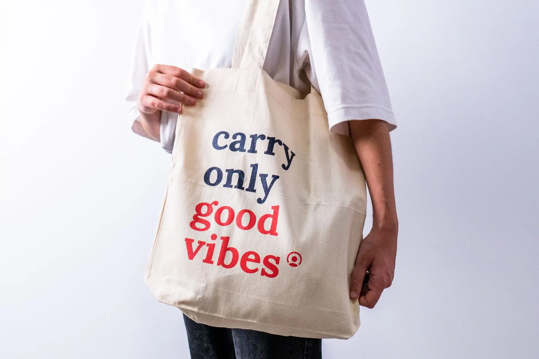 Person mit beiger Stofftasche, auf der der Spruch „carry only good vibes“ in blauer und roter Schrift steht.